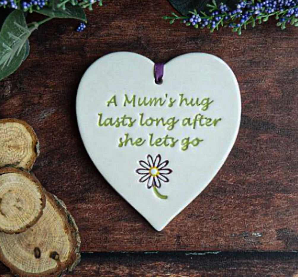 Mum Ceramic Gift Tag with a flower image and text saying "a mum's hug last ling after she lets go", surrounded by foliage