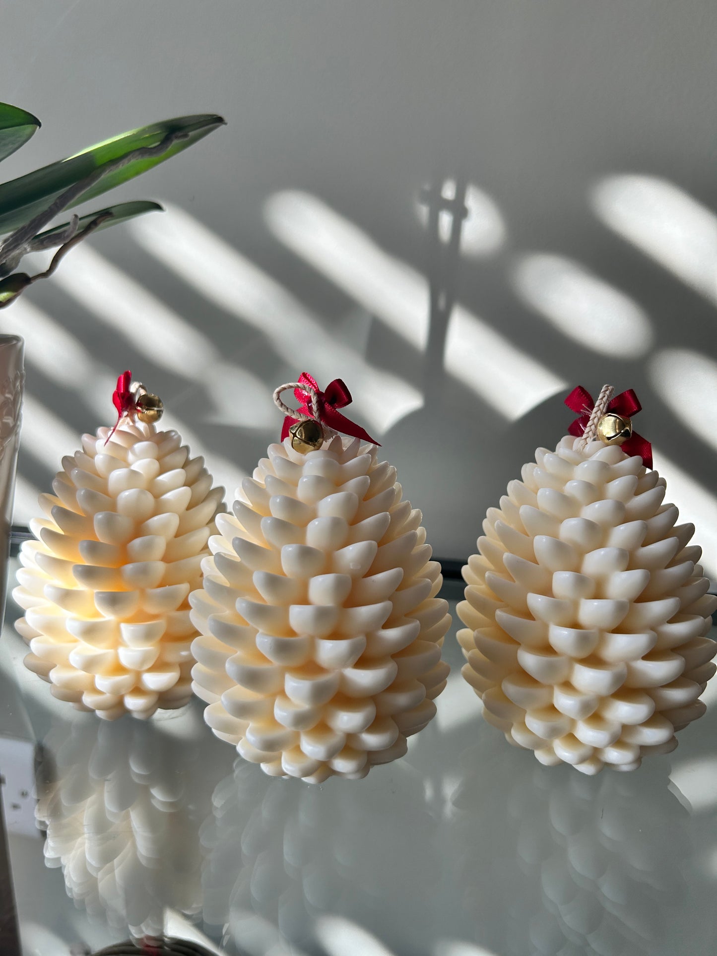3 white fir cone shaped candles with red ribbon and bells on the top