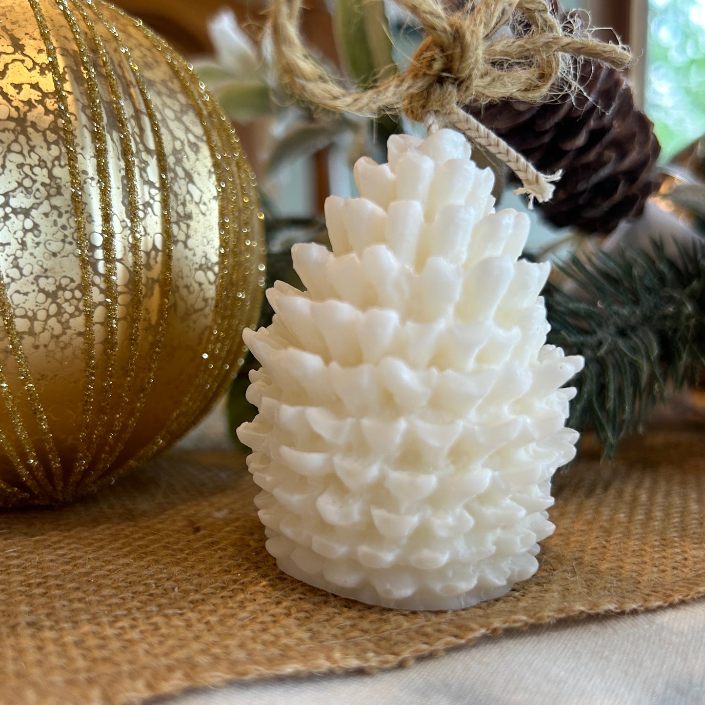 pinecones shaped candle in front of a large bauble and pine cone