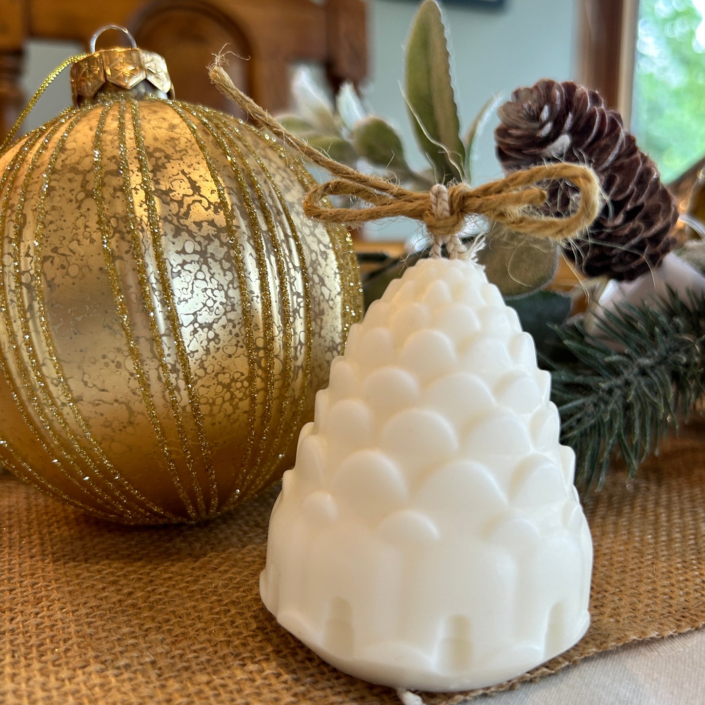 pine cone shapes candle with bow in the wick in front of large bauble and garland with pine cone