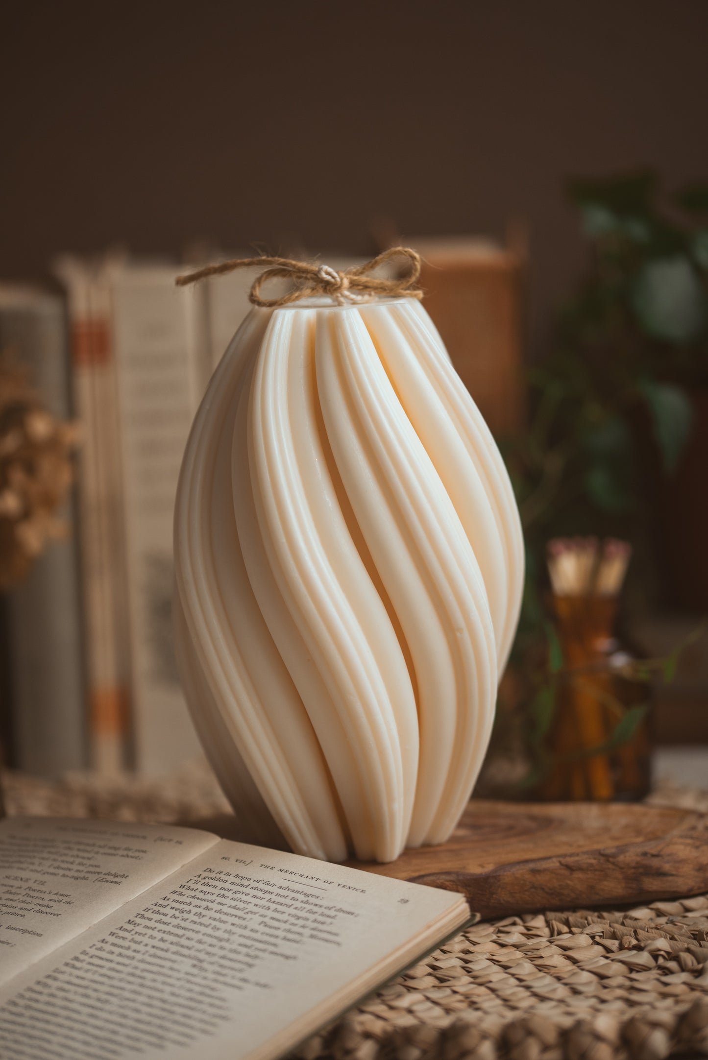  pillar candle with twisted details and books behind, there is a bow on the top of the candle with ribbon 