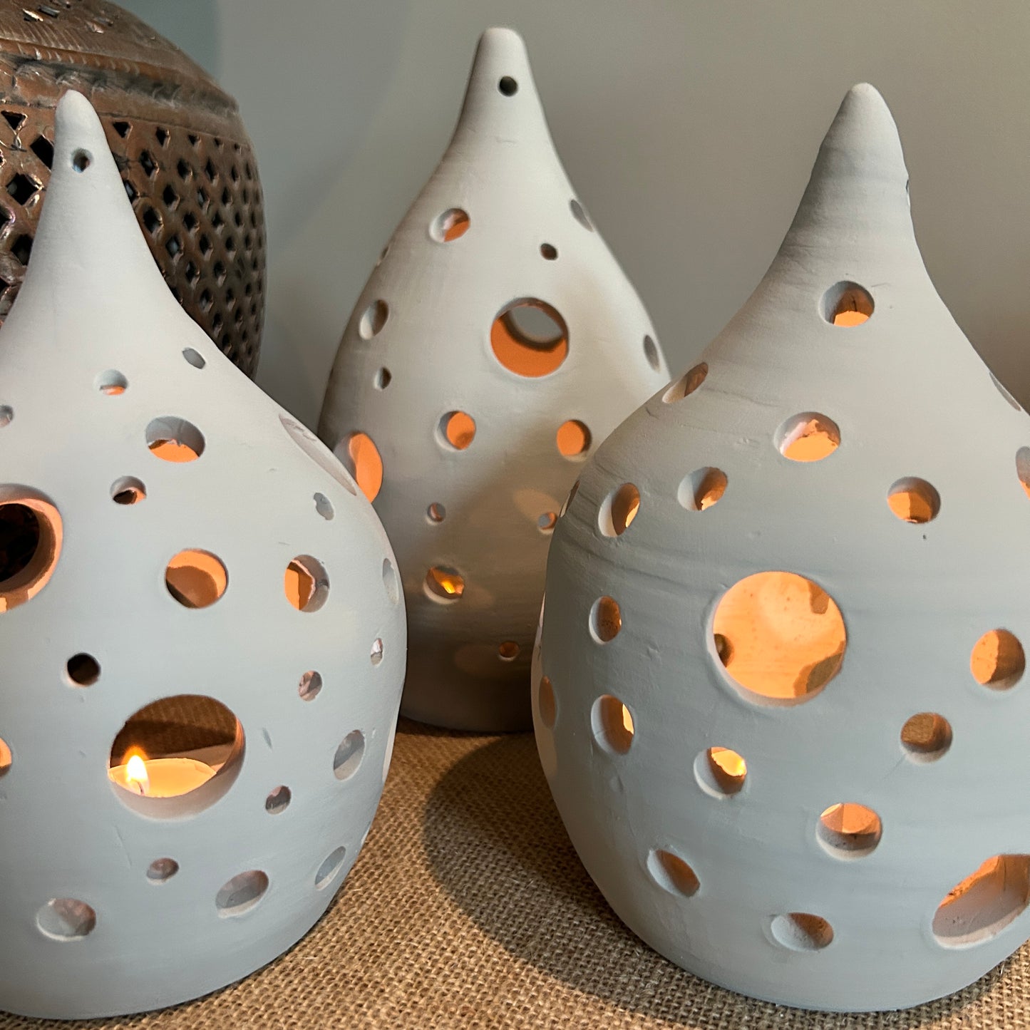 three pottery lanterns with holes across them, and lit from inside by candles 