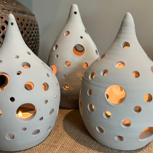 three pottery lanterns with holes across them, and lit from inside by candles 
