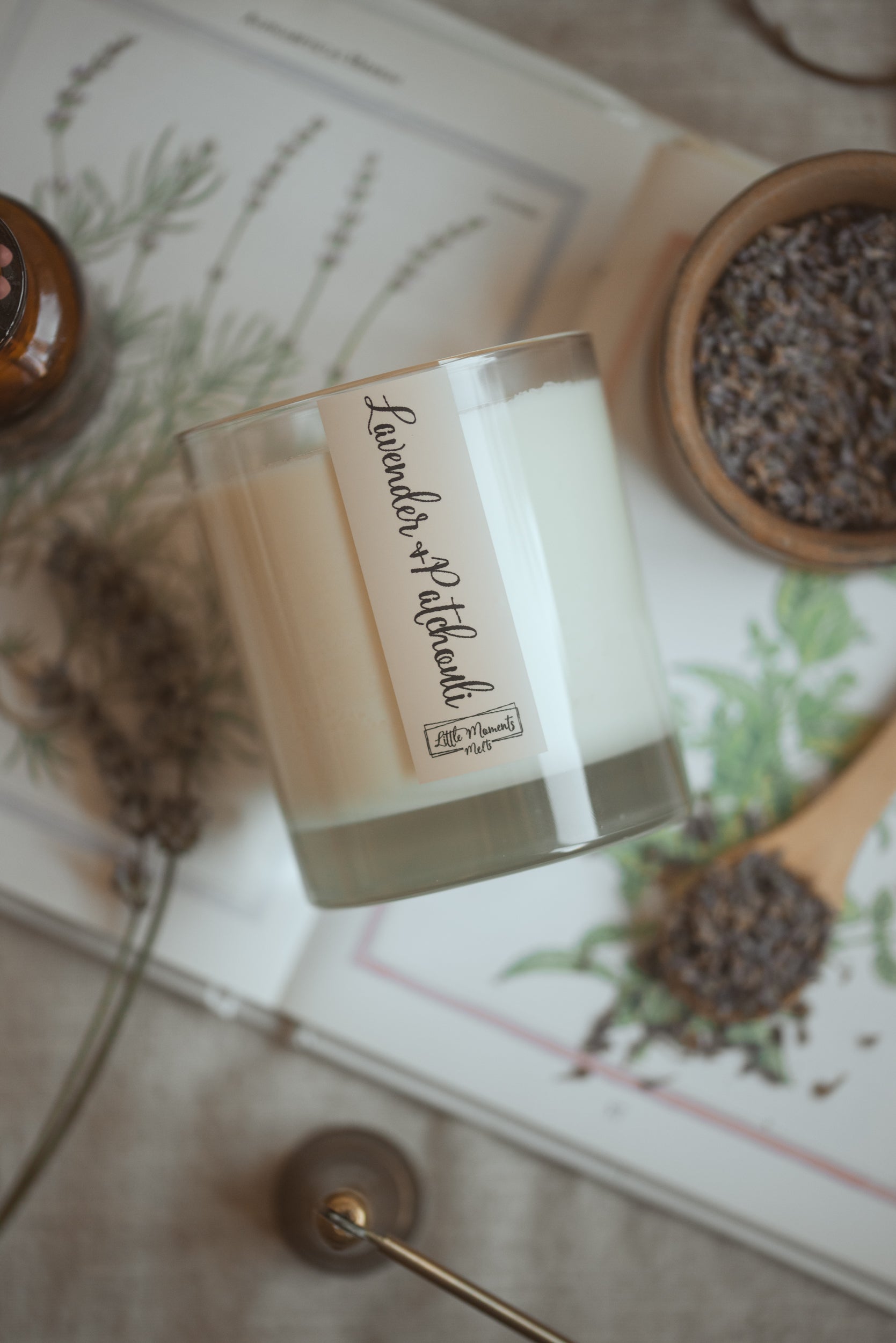 lavender and patchouli candle laid down with lavender around in a jar and on a wooden spoon 