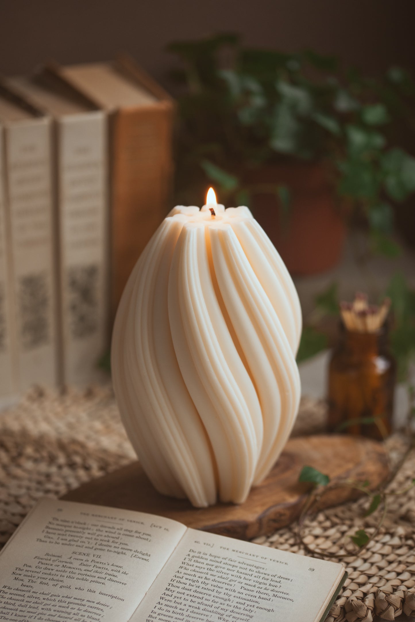 lit pillar candle  with twisted details and books behind 