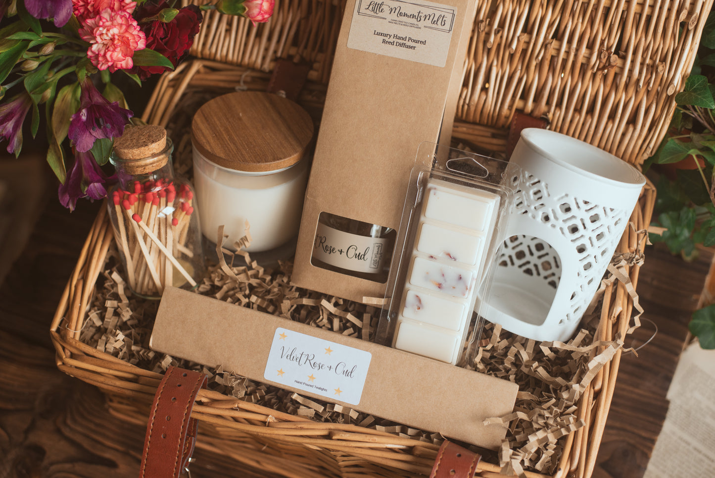 Gift basket with candles, a white wax burner and decorative items on a wooden surface.