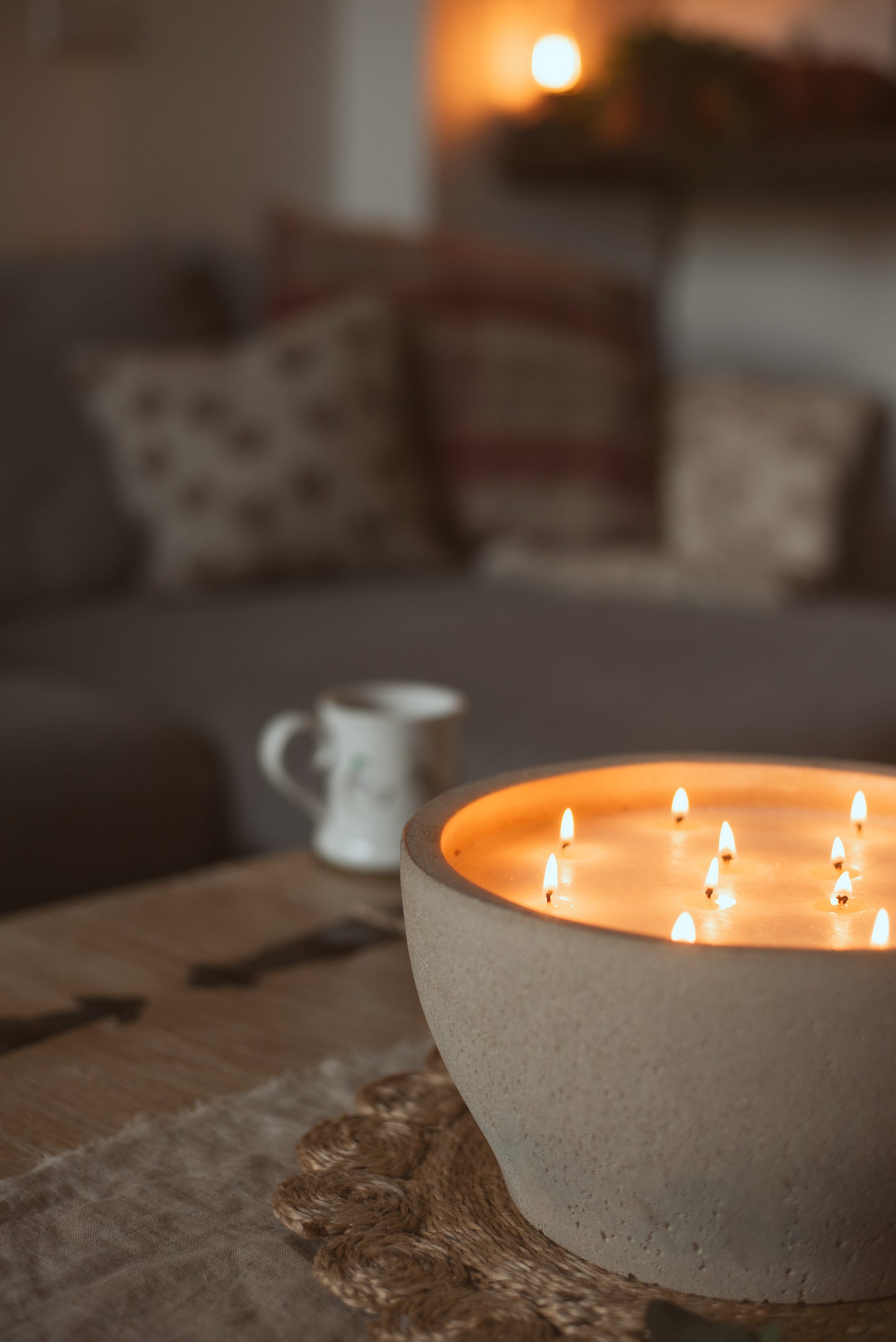 large bowl candle with 10 wicks visual and lit, with a mug and sofa behind 