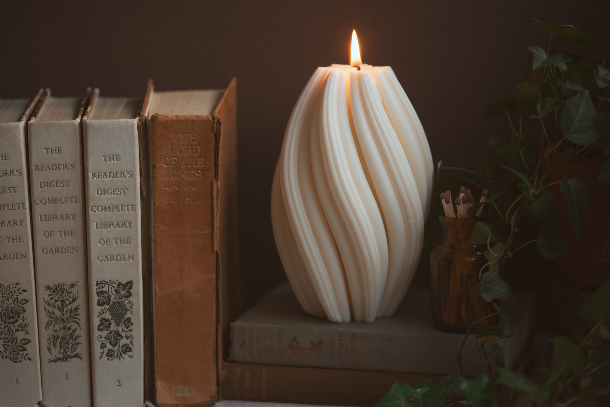 lit pillar candle with twisted details, with matches and books beside it 