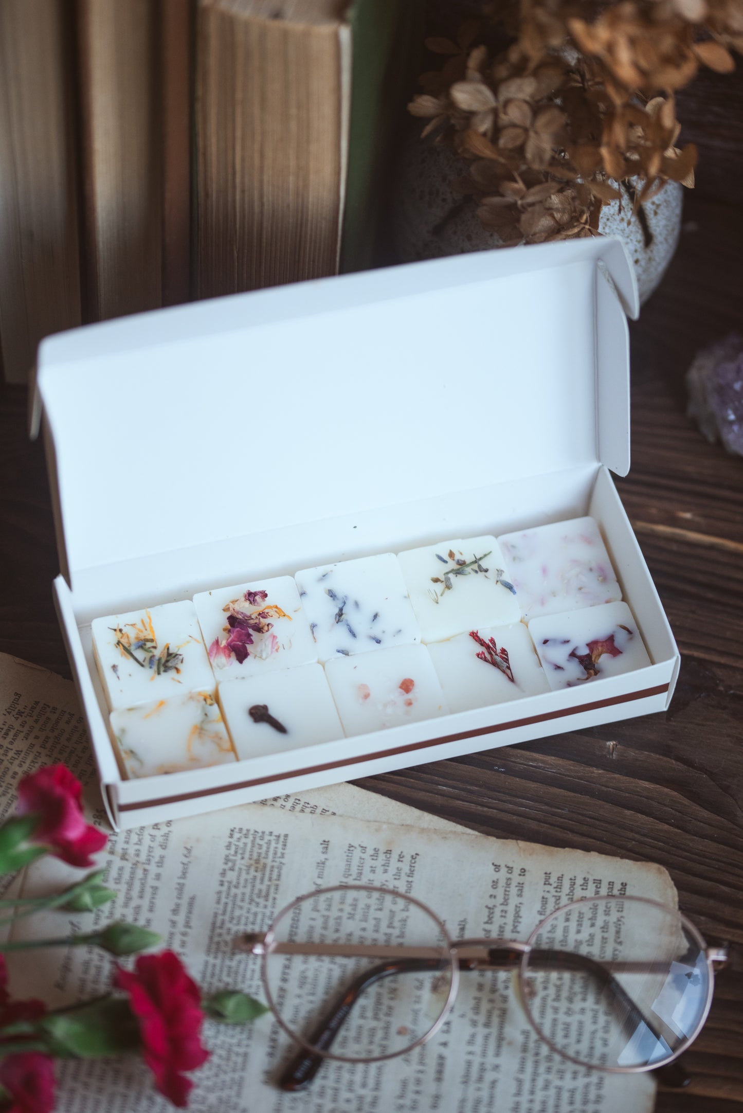 "A professional display of Little Moments Melts botanical wax melt gift boxes and reed diffusers on rustic wooden shelving at a craft fair."