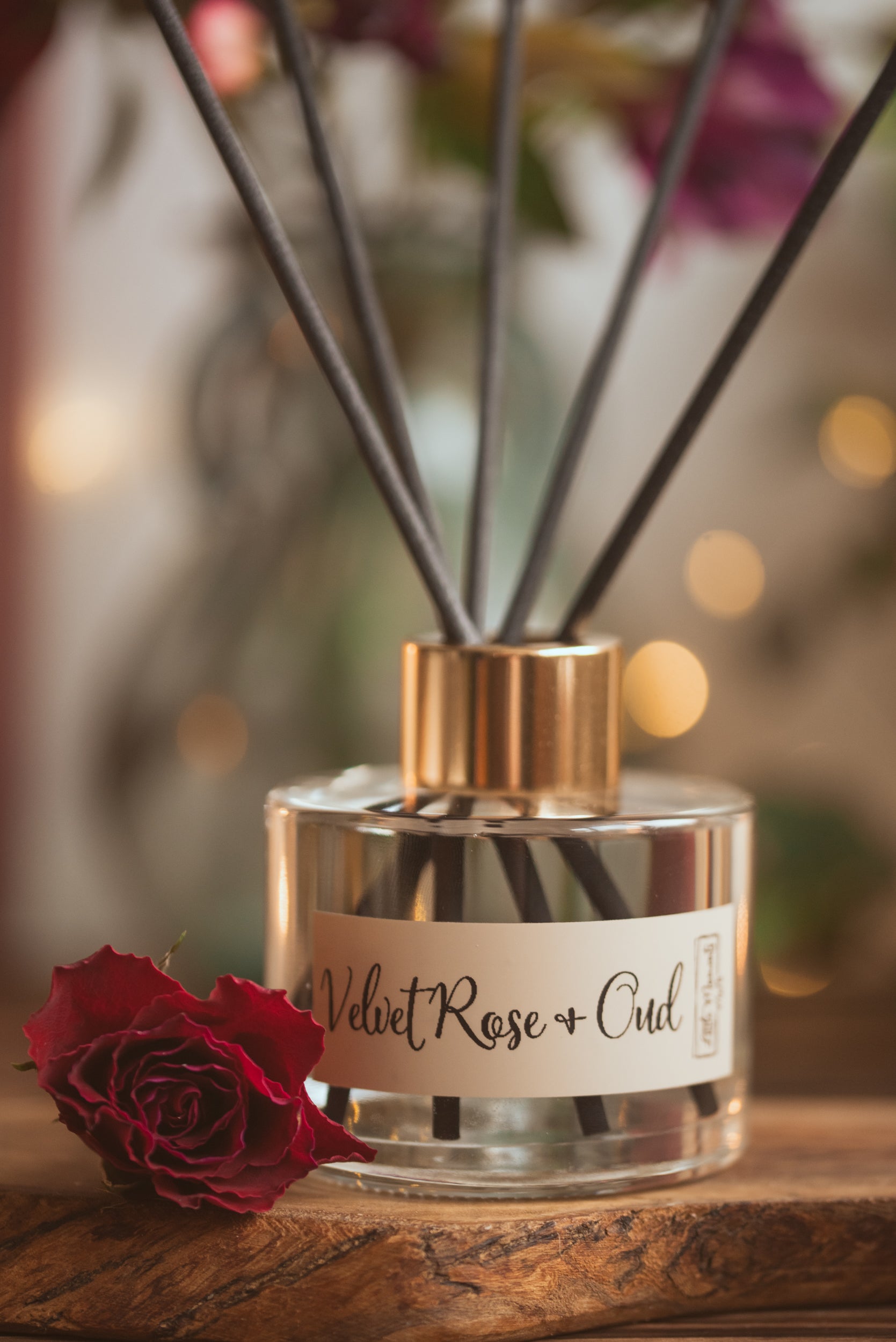 Diffuser bottle labeled 'Velvet Rose & Oud' with reeds and a red rose on a wooden surface.