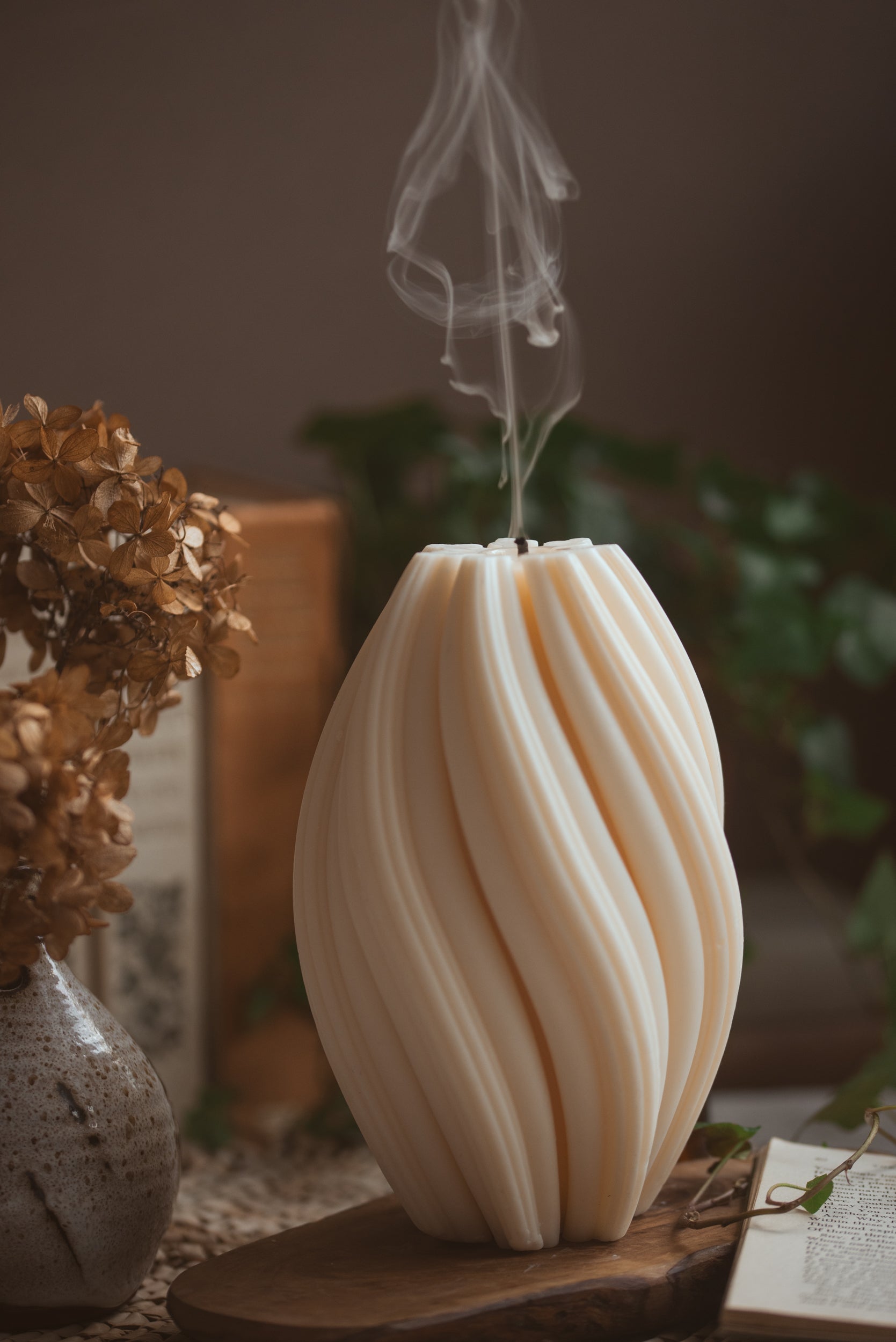  pillar candle with twisted details and books behind, just blown put and smoke rising 