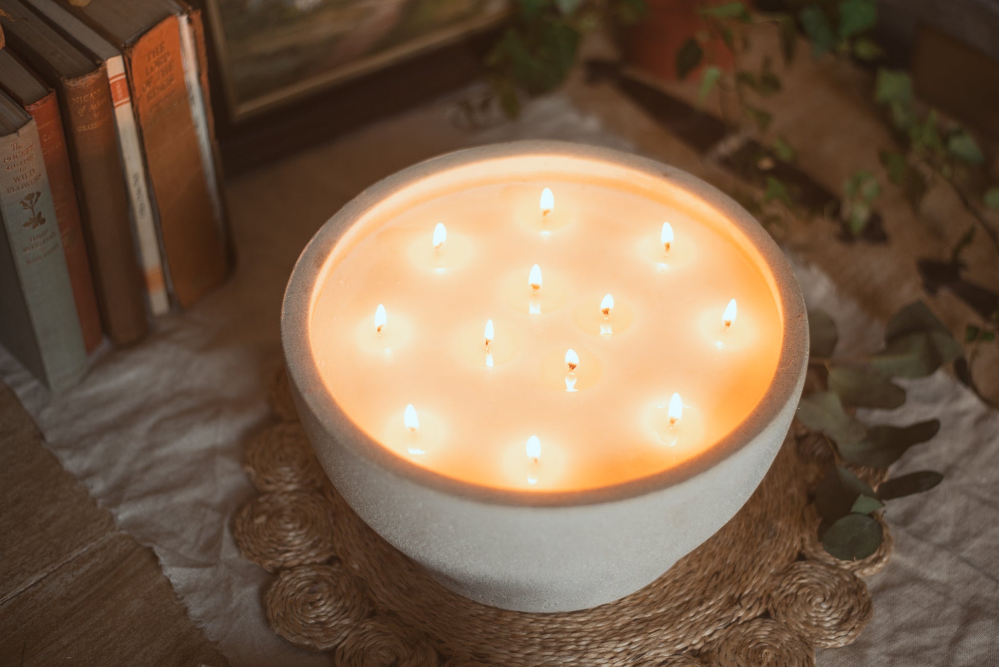 large bowl candle with 12 wicks, all wicks are lit, with a selection of books beside
