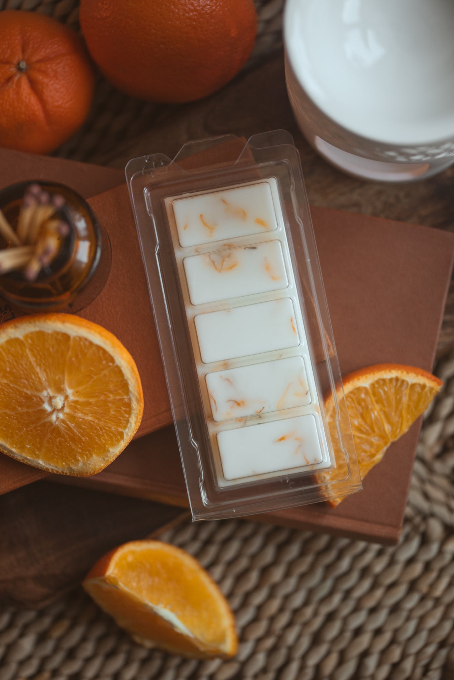 1 x wax melt snap bars surrounded by slices of fresh orange and sitting on a brown covered book