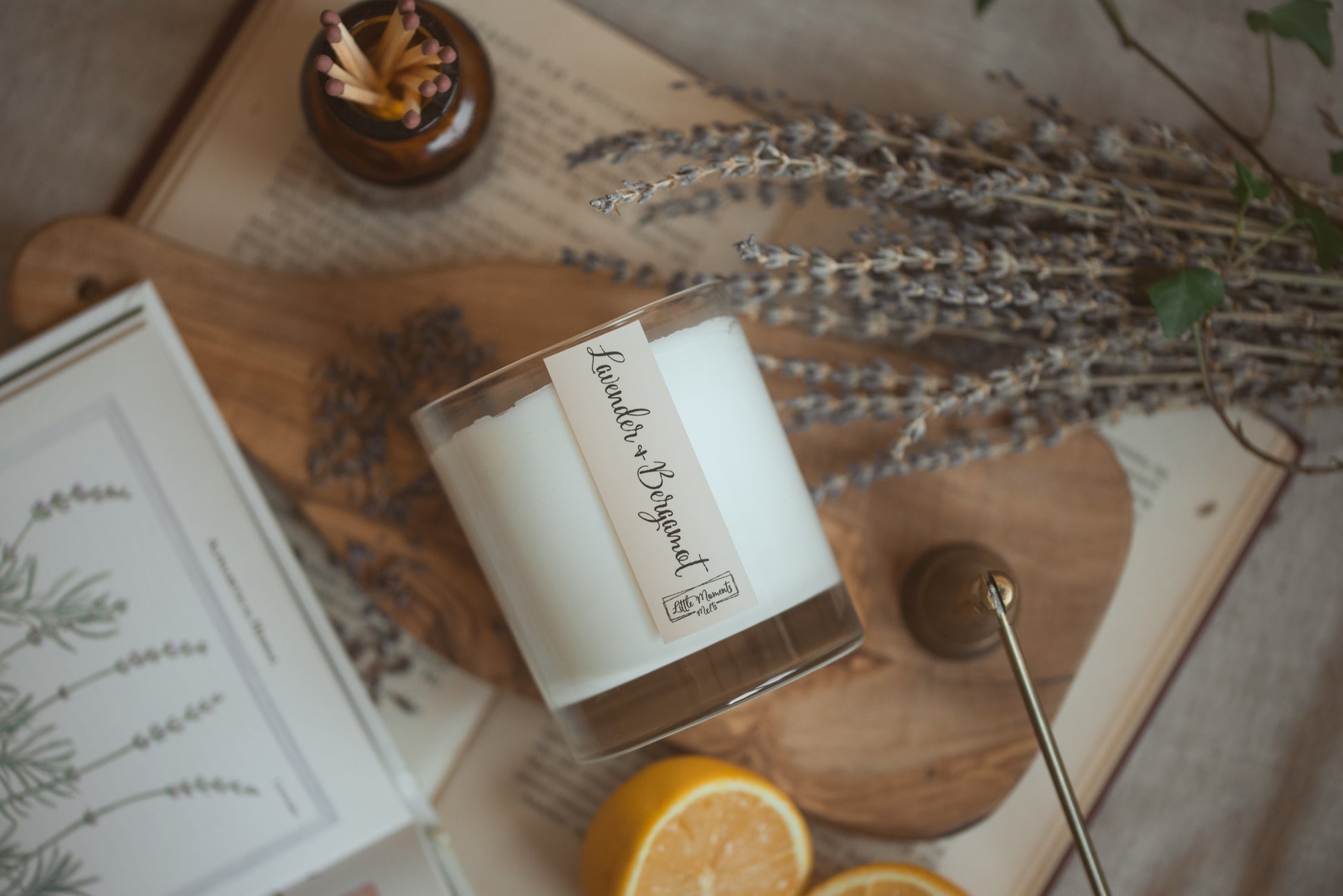 lavender and bergamot candle laid on its side with lavender, matches and oranges around the candle 
