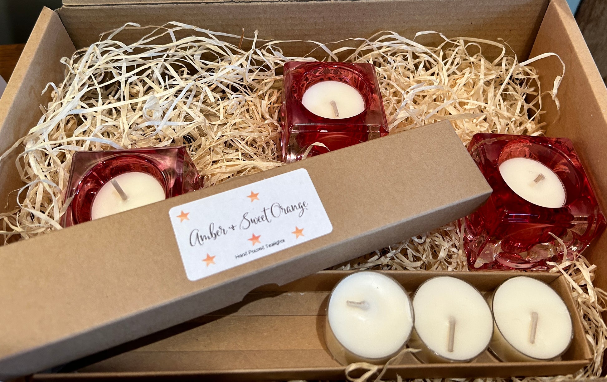 3 x pink  square  glass Tealight holders with tealight candles in a box surrounded by wooden, shredded packaging 