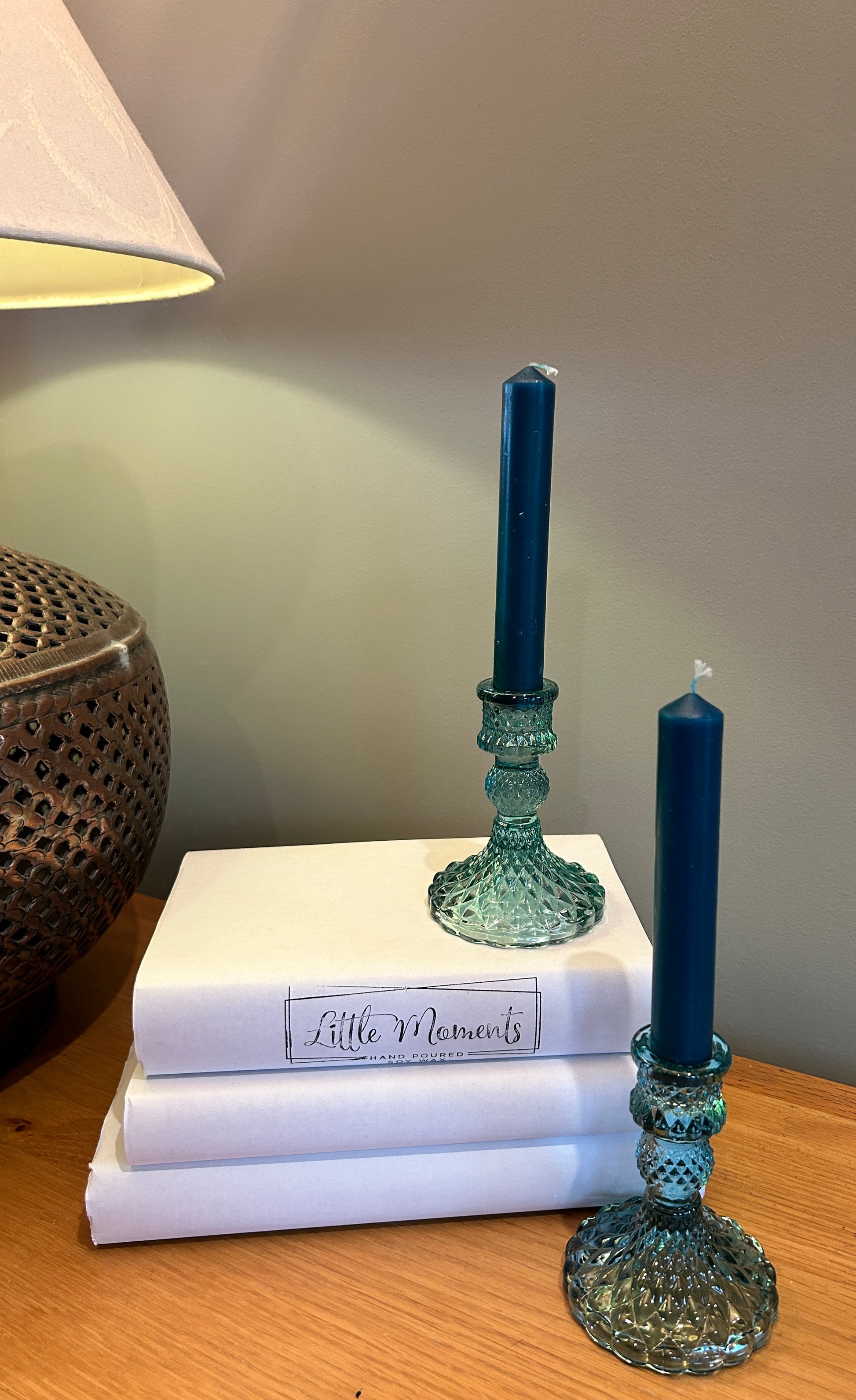 Blue glass  candlesticks with blue  dinner candles, on top of books and beside a lamp
