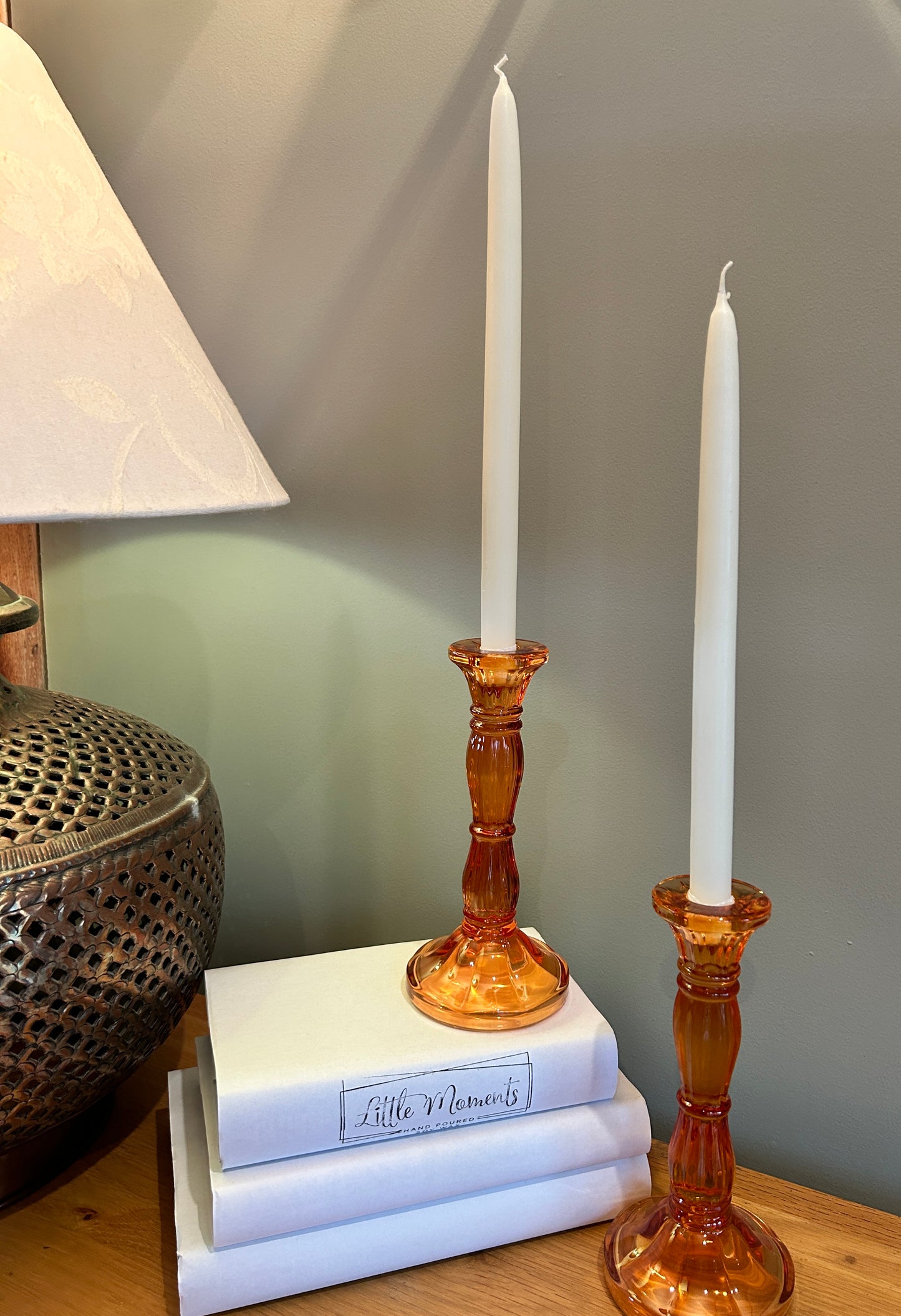 Two orange glass candlesticks with tapered dinner candles, beside a lamp and books 