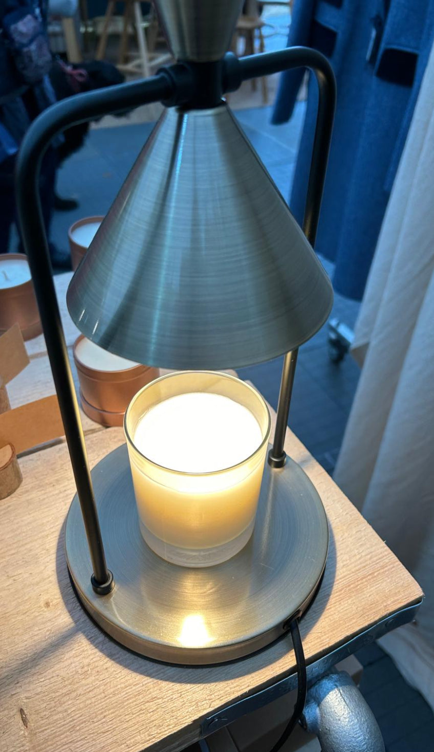 lit white candle in glass jar with lamp shade above 