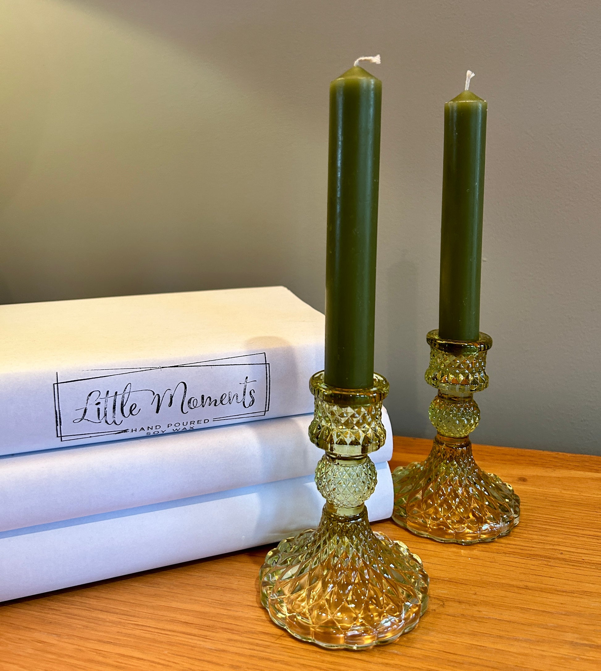 Sage green glass  candlesticks in green with green dinner candle, beside books 