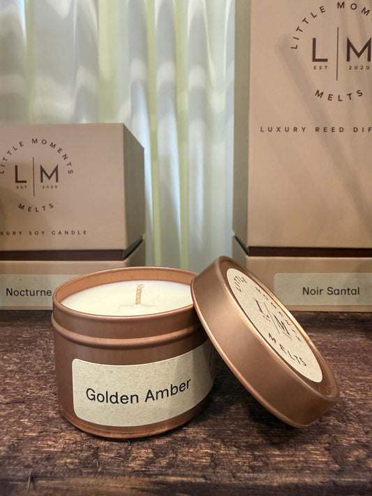 Two candle tins labeled 'Golden Amber' and 'Nocturne' with 'LM Moments Melts' branding on a wooden surface.
