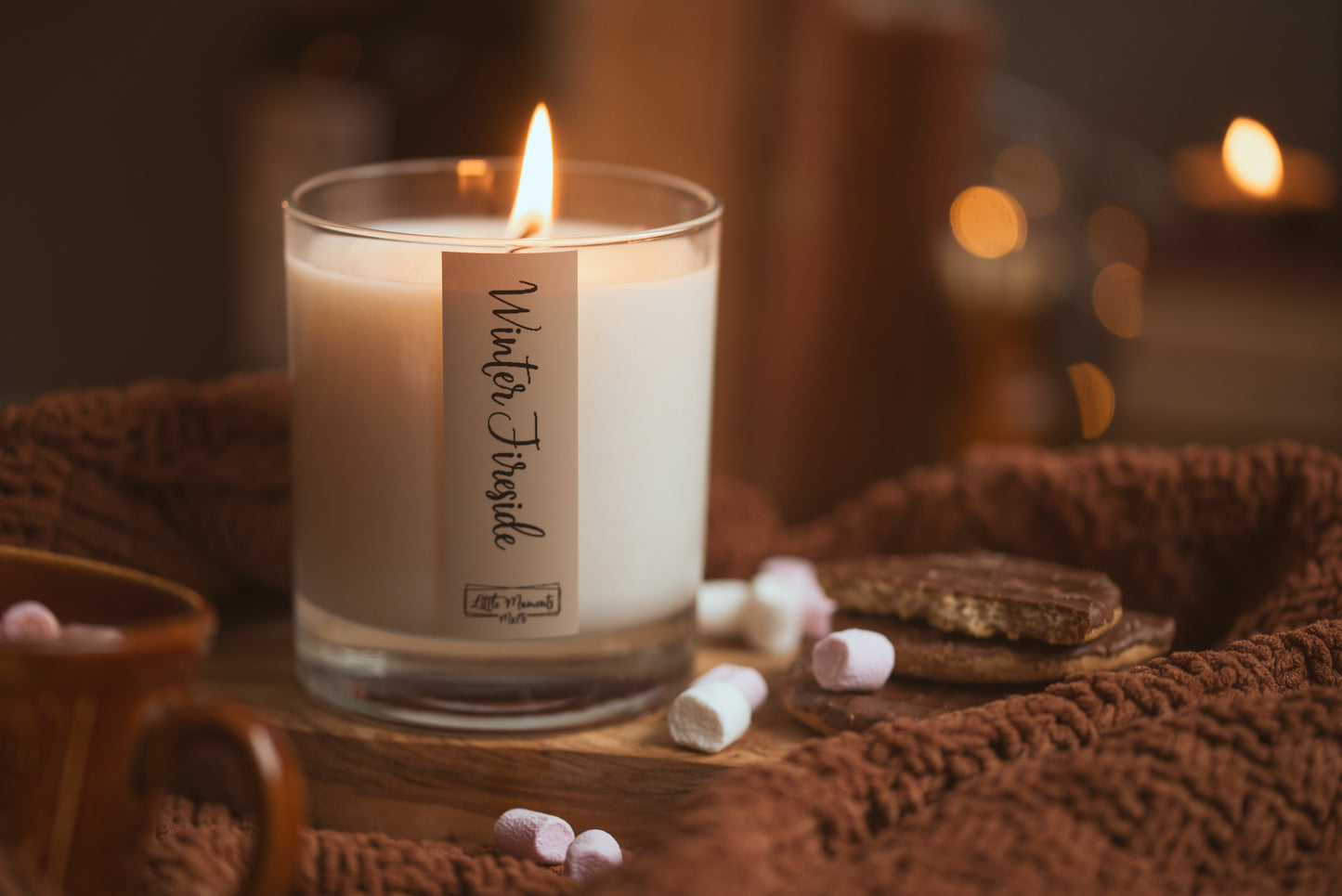 Candle labeled 'Winter Twinkle' on a woven surface with marshmallows and cookies.