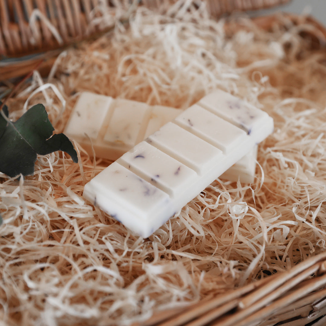 pack of hand poured soy wax melt snap bars surround by packaging shredded wooden strands with botanicals in various fragrances.